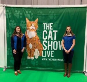 Gemini Genetics team members standing in front of a Cat Show Live banner