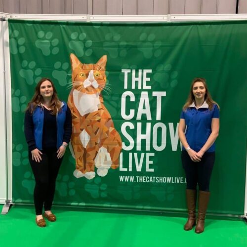 Gemini Genetics team members standing in front of a Cat Show Live banner